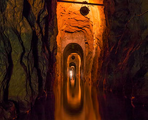 The photograph shows an illuminated adit walkway with water at the bottom.