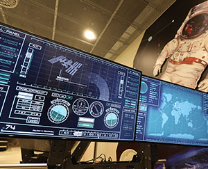 The image shows monitors displaying complex data referring to a satellite in space.