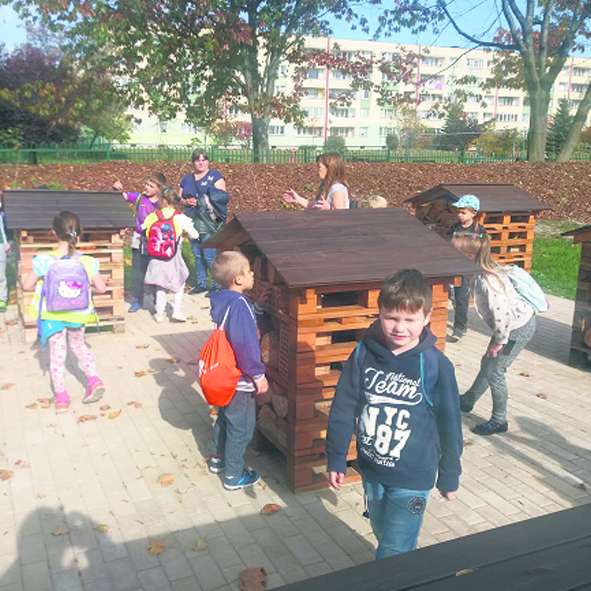 Dzieci w ogrodzie służącym do edukacji ekologicznej oglądają drewniane domki.