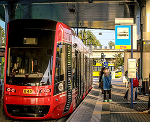 The photograph shows a tram and people at a covered stop.