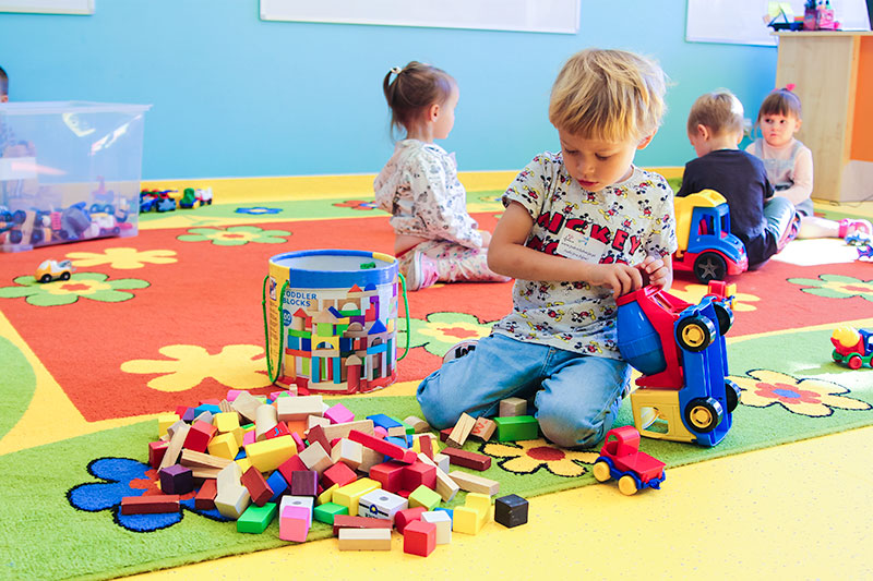 Fotografia przedstawia chłopczyka bawiącego się kolorowymi klockami na dywanie.