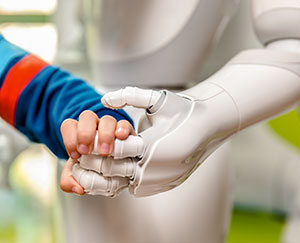 The photograph shows a child's hand clutching the hand of a robot.