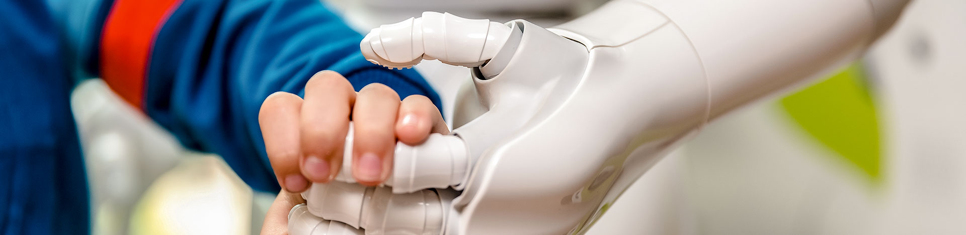Fotografia przedstawia dłoń dziecka, która ściska dłoń robota.