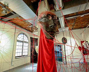 The photograph shows an element of the exhibition. It is a mask, suspended around red strings.