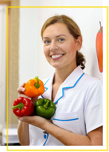 The photograph shows Katarzyna Stefaniak-Podeszwa, owner of the FitBalans company from Żory. A woman in a white coat is holding multicoloured peppers. Behind her is a wall where identical peppers are painted.