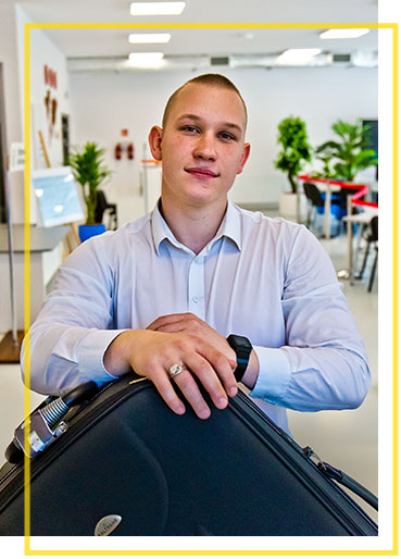 Fotografia przedstawia Wojciecha Adamczyka, ucznia klasy o profilu eksploatacja portów i terminali lotniczych Technikum nr 4 Transportowego CKZIU w Sosnowcu. Chłopak trzyma na walizce. Za nim znajduje się bramka do wykrywania metali.
