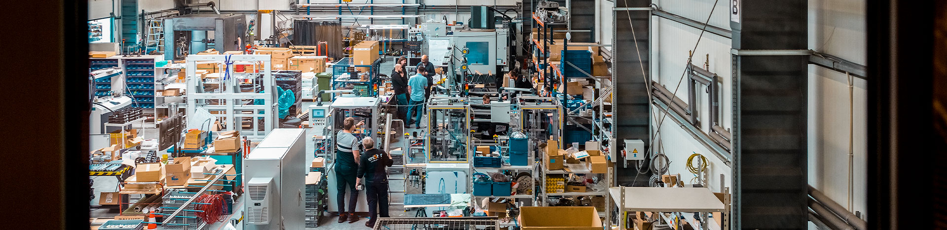 Fotografia przedstawia halę w firmie. Widoczne są maszyny i pracownicy.