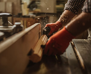 The photograph shows red-gloved hands operating a carpenter's machine.
