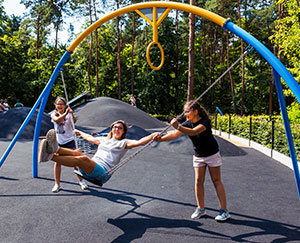 The photograph shows two girls moving a swing on which a woman is sitting.