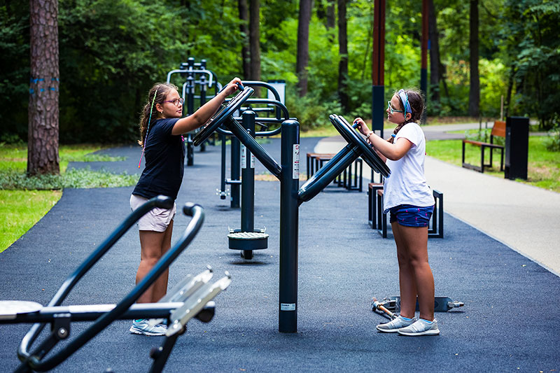 Fotografia przedstawia dwie dziewczynki, które ćwiczą na siłowni plenerowej.