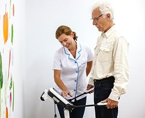 Fotografia przedstawia mężczyznę stojącego na urządzeniu elektronicznym przypominającym wagę oraz kobietę w białym fartuchu, która wykonuje badanie.
