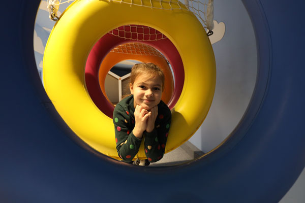 Fotografia przedstawia uśmiechniętą dziewczynkę leżącą w kolorowym tunelu.