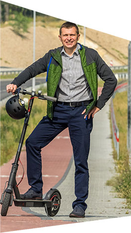 Fotografia przedstawia Tomasza Kulpoka, mieszkańca Rudy Śląskiej, który pozuje do zdjęcia z hulajnogą, na ścieżce rowerowej przy trasie N-S.