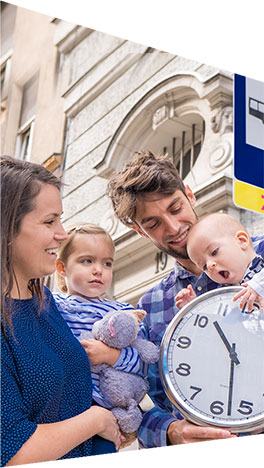 Fotografia przedstawia młode małżeństwo - Anię i Mateusza Jędrzejewskich, którzy pozują do fotografii z dwójką swoich małych dzieci oraz zegarem ściennym, na jednym z przystanków autobusowych.