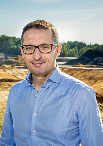 The photograph shows Piotr Kuczera, the mayor of Rybnik, against the background of the construction of the Racibórz-Pszczyna road, a section in Rybnik. You can see a viaduct and a route, which has been marked but not yet covered with asphalt. The mayor is wearing glasses and a blue shirt. He’s smiling. The photo comes from the archives of the beneficiary.