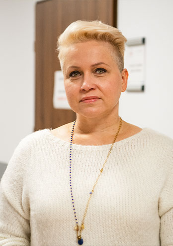 Fotografia przedstawia Iwonę Łuczak, koordynatora projektów unijnych w Hospicjum Sosnowieckim imienia świętego Tomasza Apostoła. Kobieta ma krótkie blond włosy. Stoi w korytarzu centrum. Autorem zdjęcia jest Maciej Motylewski.