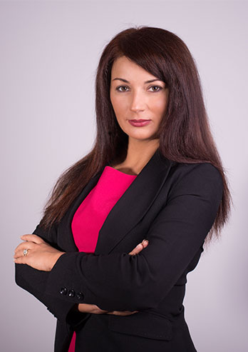 Fotografia przedstawia Izabelę Domogałę, członka zarządu województwa śląskiego. Kobieta ma długie, proste, czarne włosy i czarny żakiet. Stoi, z założonymi rękami. Zdjęcie pochodzi z archiwum prywatnego.