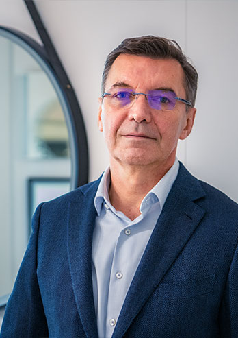 The photograph presents Jacek Czogalla, the owner of the company. He’s wearing a shirt, jacket and glasses. You can see mirrors in the background. The photo was taken by Dominik Wójcik.