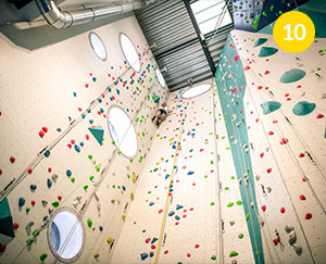 The photograph is taken from the floor level and shows one of the climbing walls in its full glory. You can see a lot of colorful support points for the climbers. Almost at the top, you can see a woman climbing. The photo was taken by Dominik Wójcik.