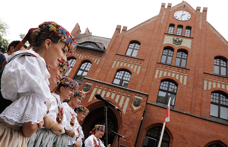 Zespół folklorystyczny w śląskich strojach ludowych na tle Muzeum Powstań Śląskich w Świętochłowicach
