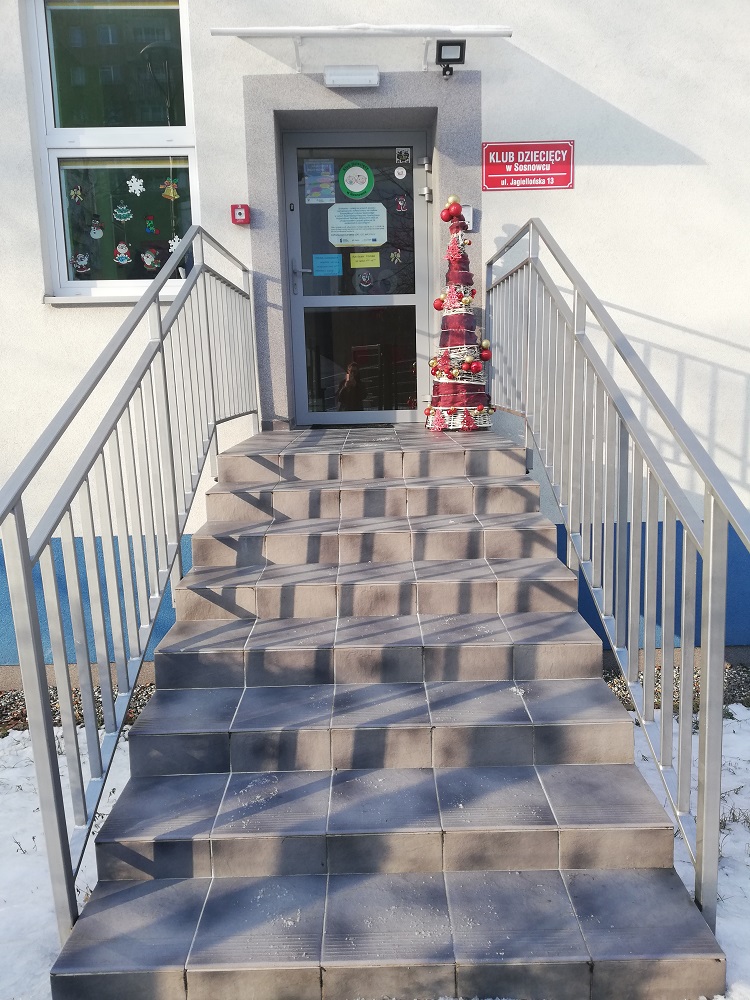 Wejście do budynku przy ulicy Jagiellońskiej po renowacji - w nowopowstałym klubie dziecięcym odrestaurowano schody, zamontowano nowe barierki i drzwi, bezpośrednio nad wejściem zamontowano oświetlenie, a tuż przy drzwiach alarm przeciwpożarowy